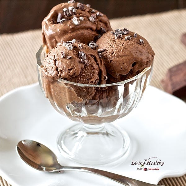 clear glass dish with three scoops of paleo chocolate ice cream topped with cacao nibs with spoon in foreground 