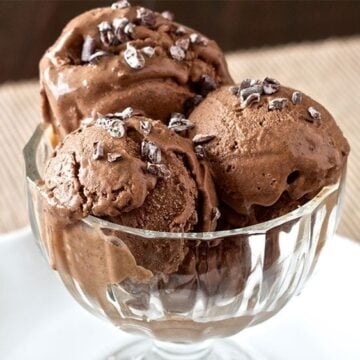 clear glass dish with three scoops of paleo chocolate ice cream topped with cacao nibs