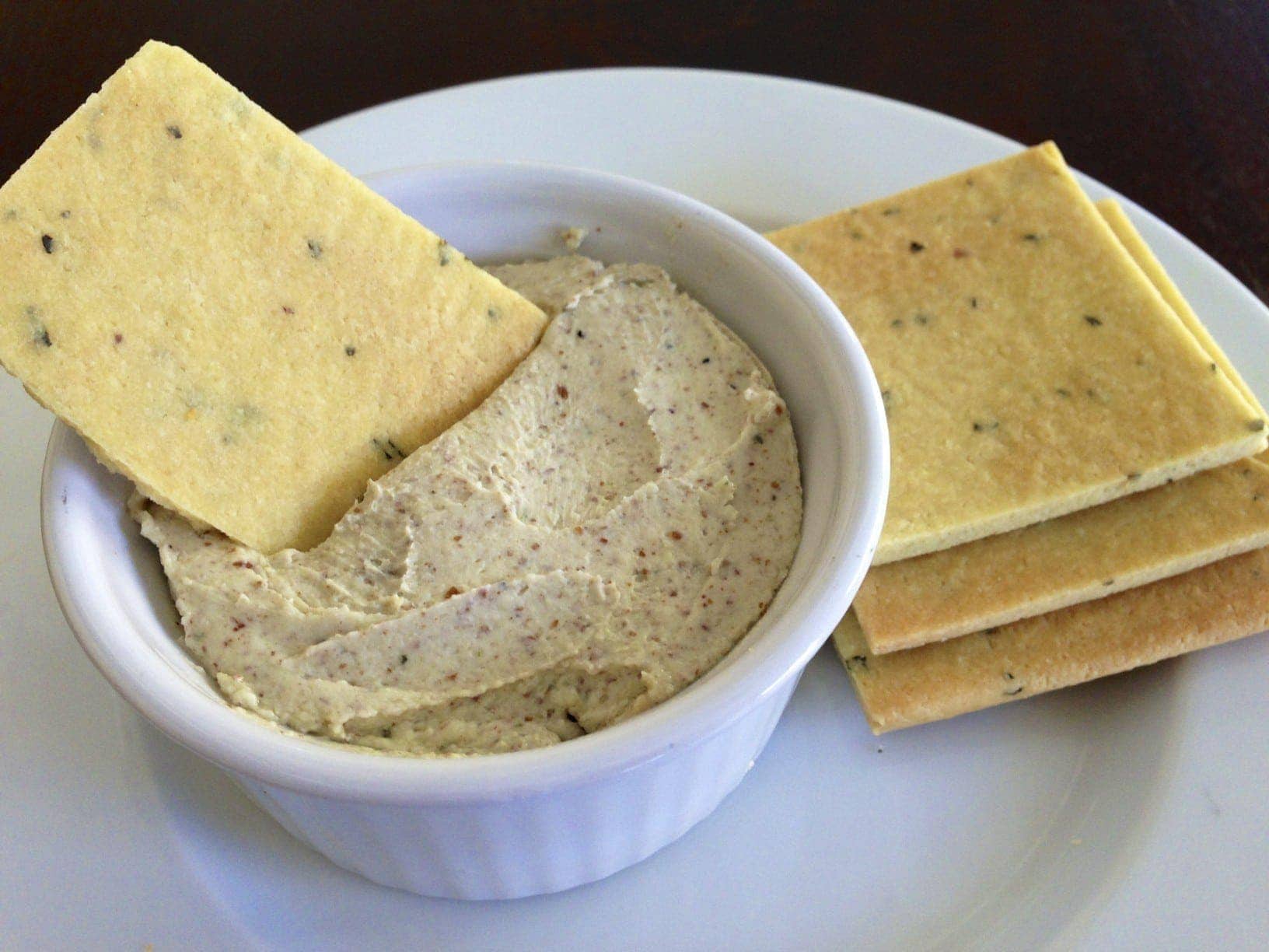 plate of homemade gluten free basil crackers next to a small serving dish with roasted garlic basil cheese dip