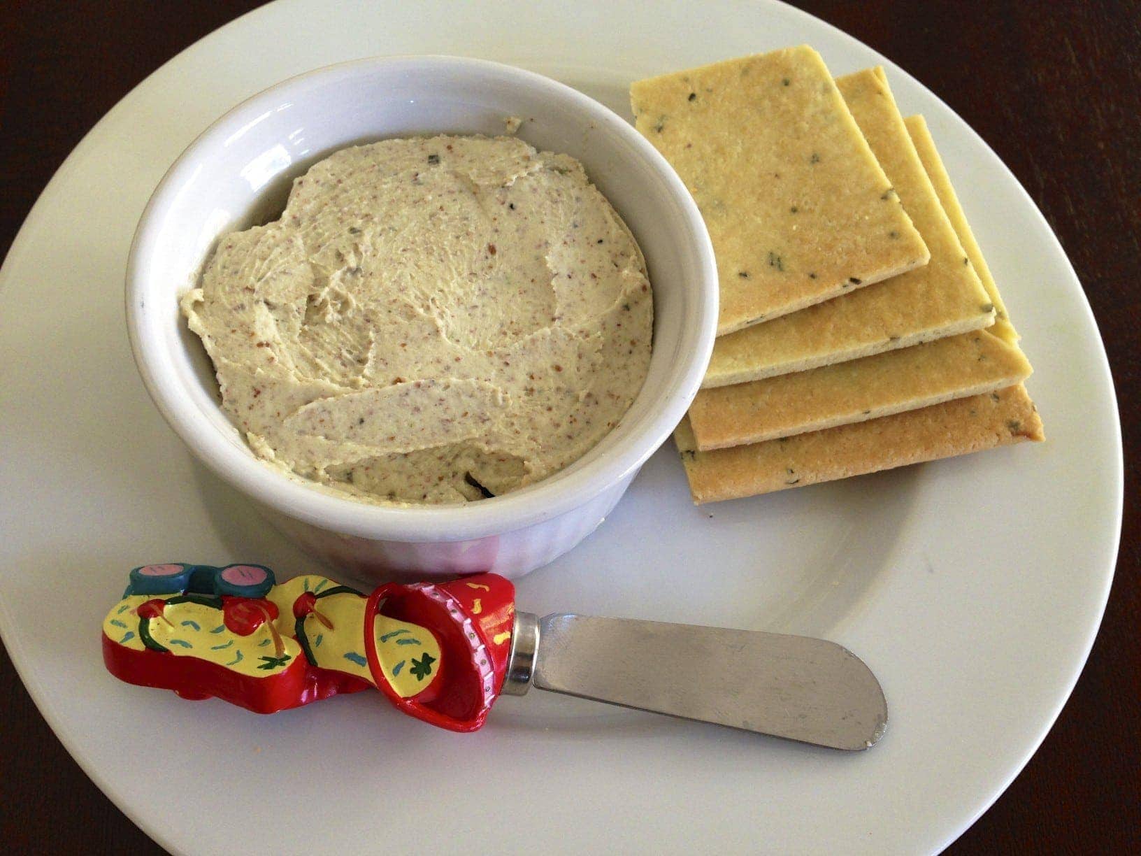 plate of homemade gluten free basil crackers next to a small serving dish with roasted garlic basil cheese dip