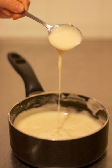 cooking pan filled with sauce to make Brazilian chocolate truffle with a spoon above dripping sauce into pan