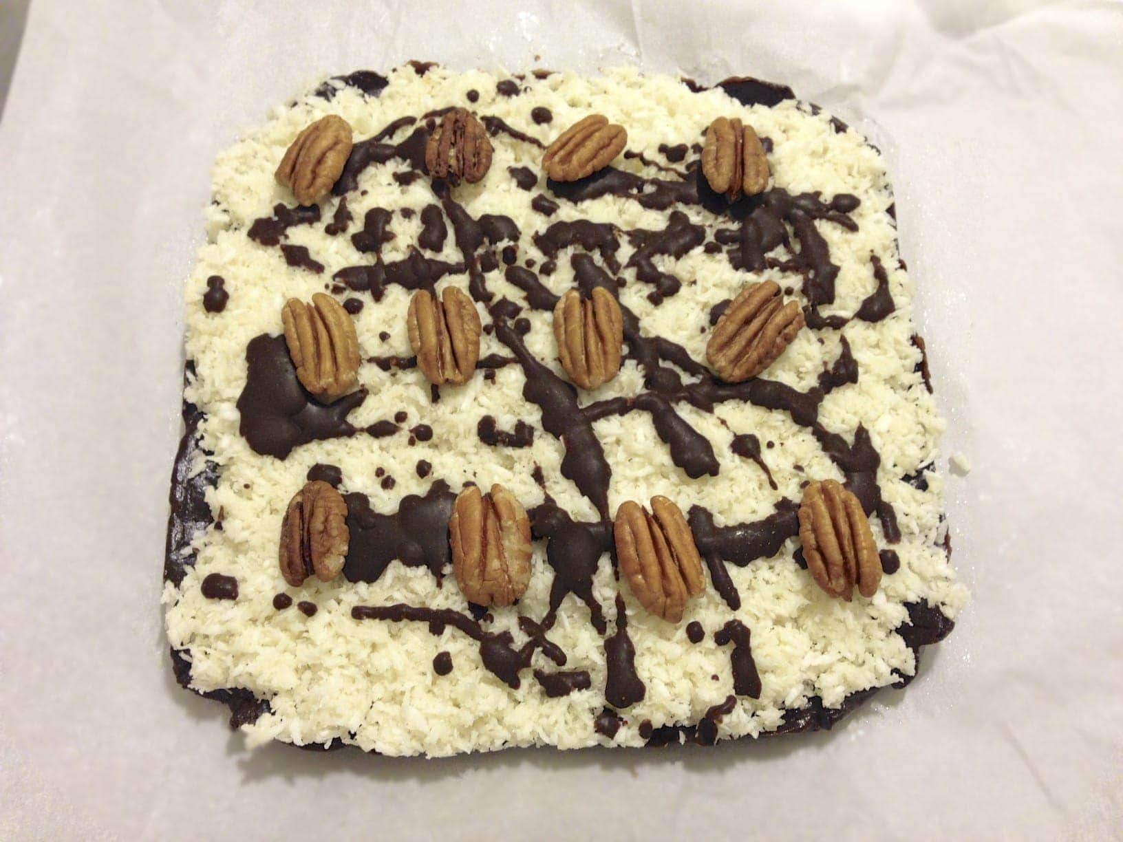 large square paleo chocolate coconut bar topped with pecans drizzled with chocolate