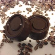 close up of two round pieces of homemade 84 percent dark chocolate with pieces of cacao nibs all around