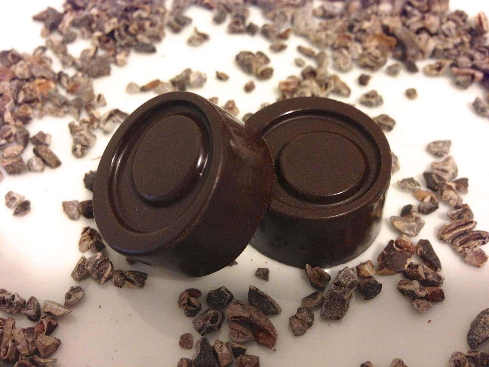 close up of two round pieces of homemade 84 percent dark chocolate with pieces of cacao nibs all around 