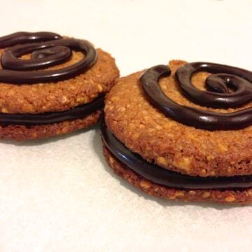close up of two pecan cookies filled with chocolate and topped with a chocolate swirl