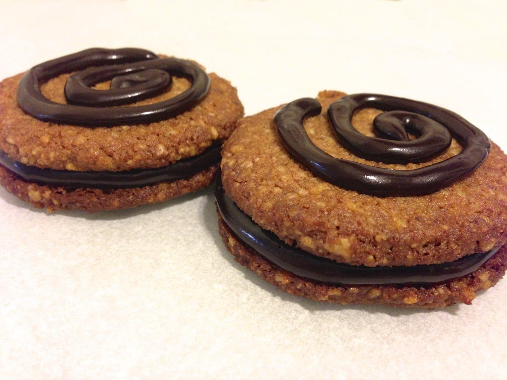 close up of two pecan cookies filled with chocolate and topped with a chocolate swirl