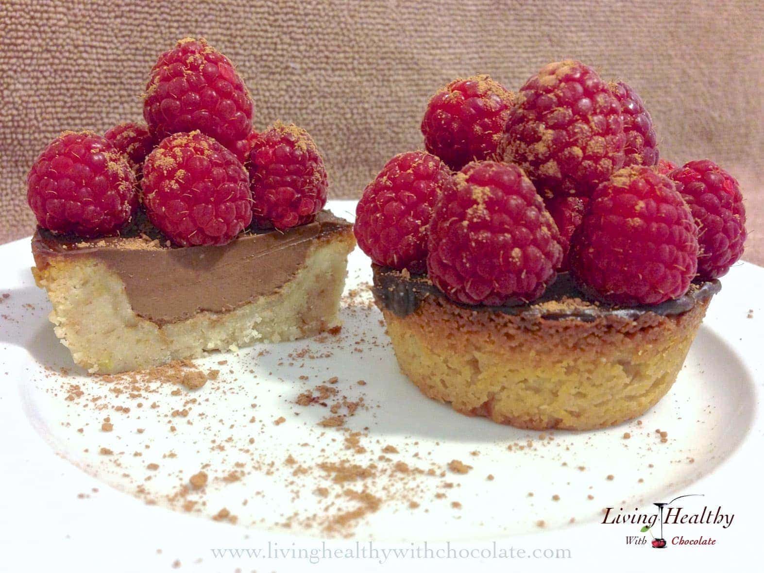 close up of two raspberry chocolate tarts dusted with cacao powder with one cut in half showing inside texture