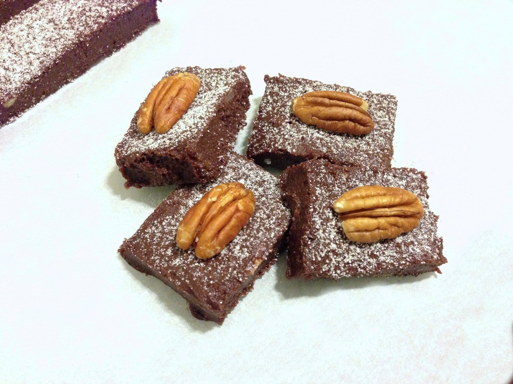 close up of four pieces of chocolate cherry fudge bars topped with one single pecan