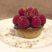 close up raspberry chocolate tart dusted with cacao powder on a round white plate