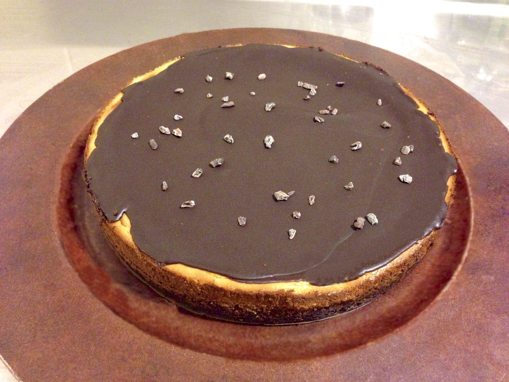 close up of large round paleo chocolate cheesecake topped with pieces of cacao nibs