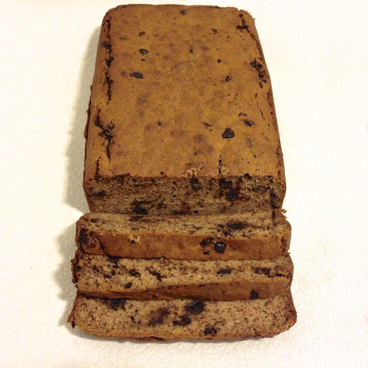 loaf of chocolate chip banana bread with three slices cut and laying down in front of the loaf