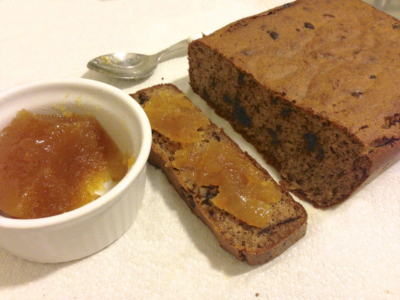 loaf of paleo chocolate chip banana bread with a small white dish on the left with orange jelly