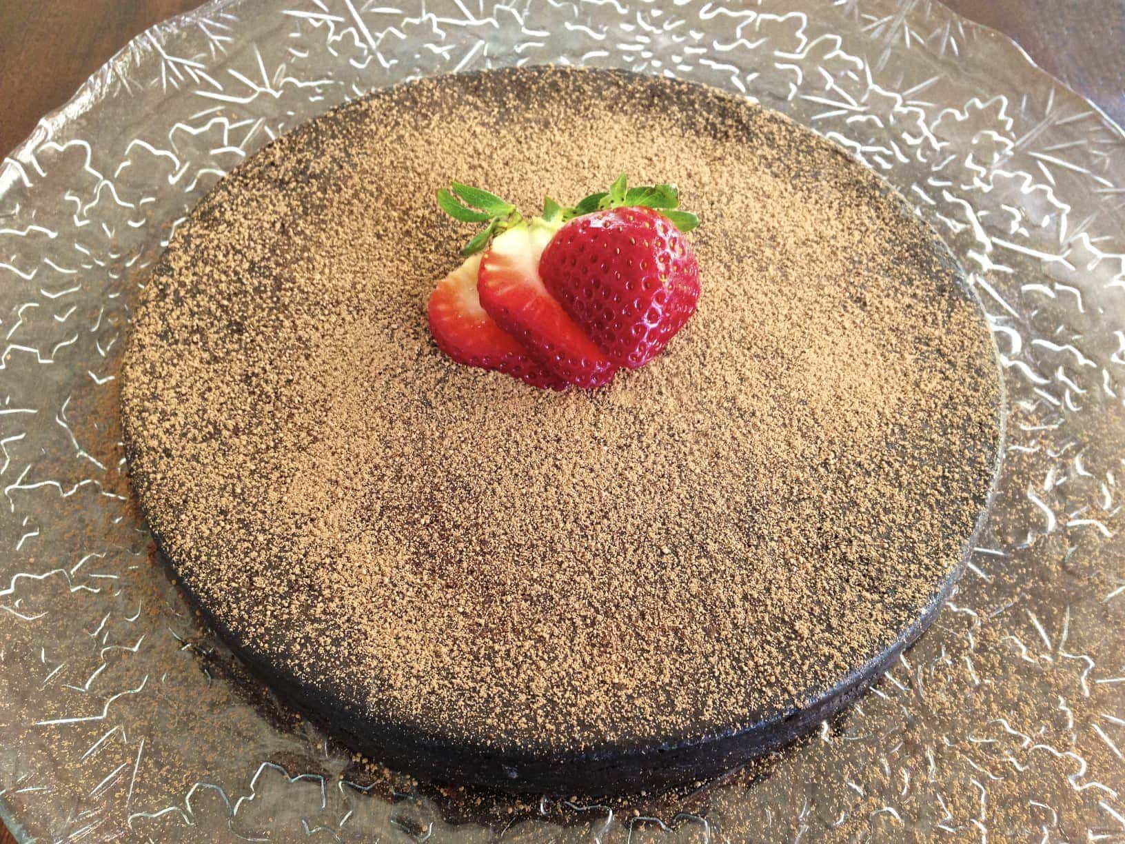 large round flourless chocolate torte dusted in cacao powder and topped with slices of fresh strawberries 