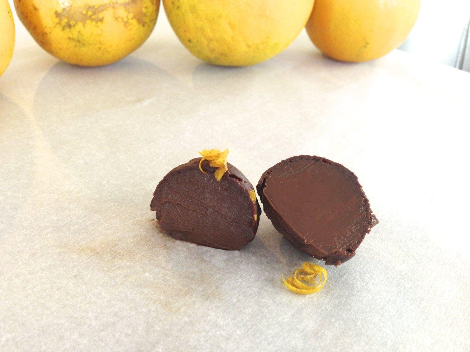 close up of dark chocolate orange truffle cut in half with three oranges in background 