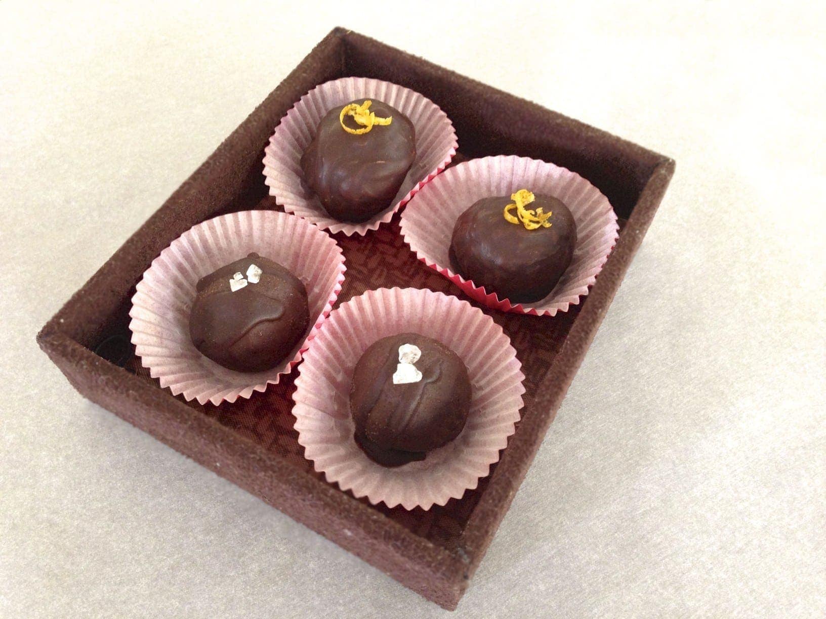 four handmade chocolate truffles in red paper cups sitting in a square serving dish