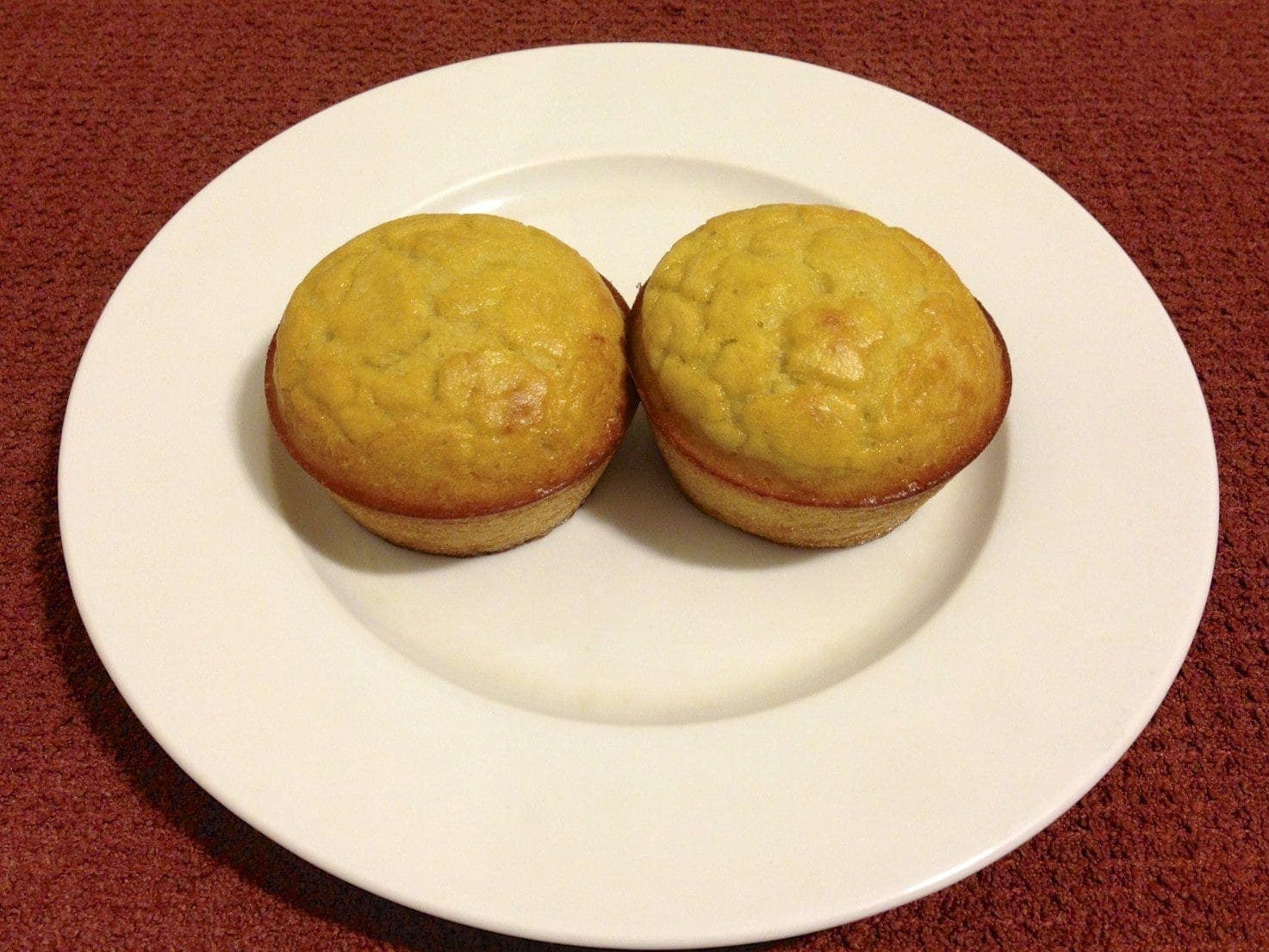 two coconut flour orange muffins on a round white plate