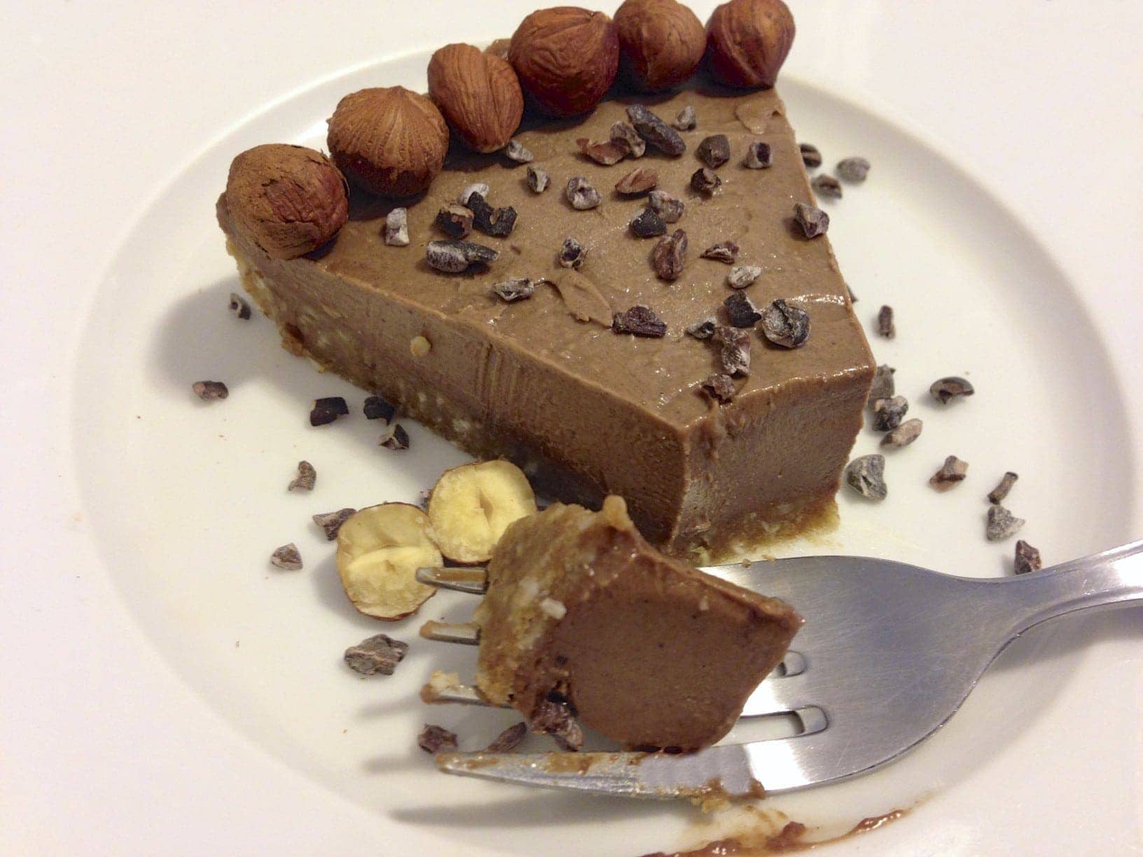 single slice of paleo hazelnut chocolate pie topped with cacao nibs and a fork in foreground with one bite resting on fork
