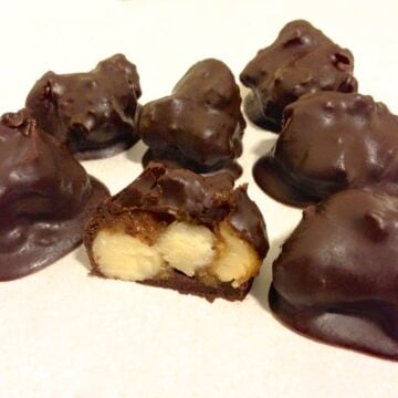 close up of several chocolate covered paleo macadamia nut clusters with one piece cut in half showing the inside texture