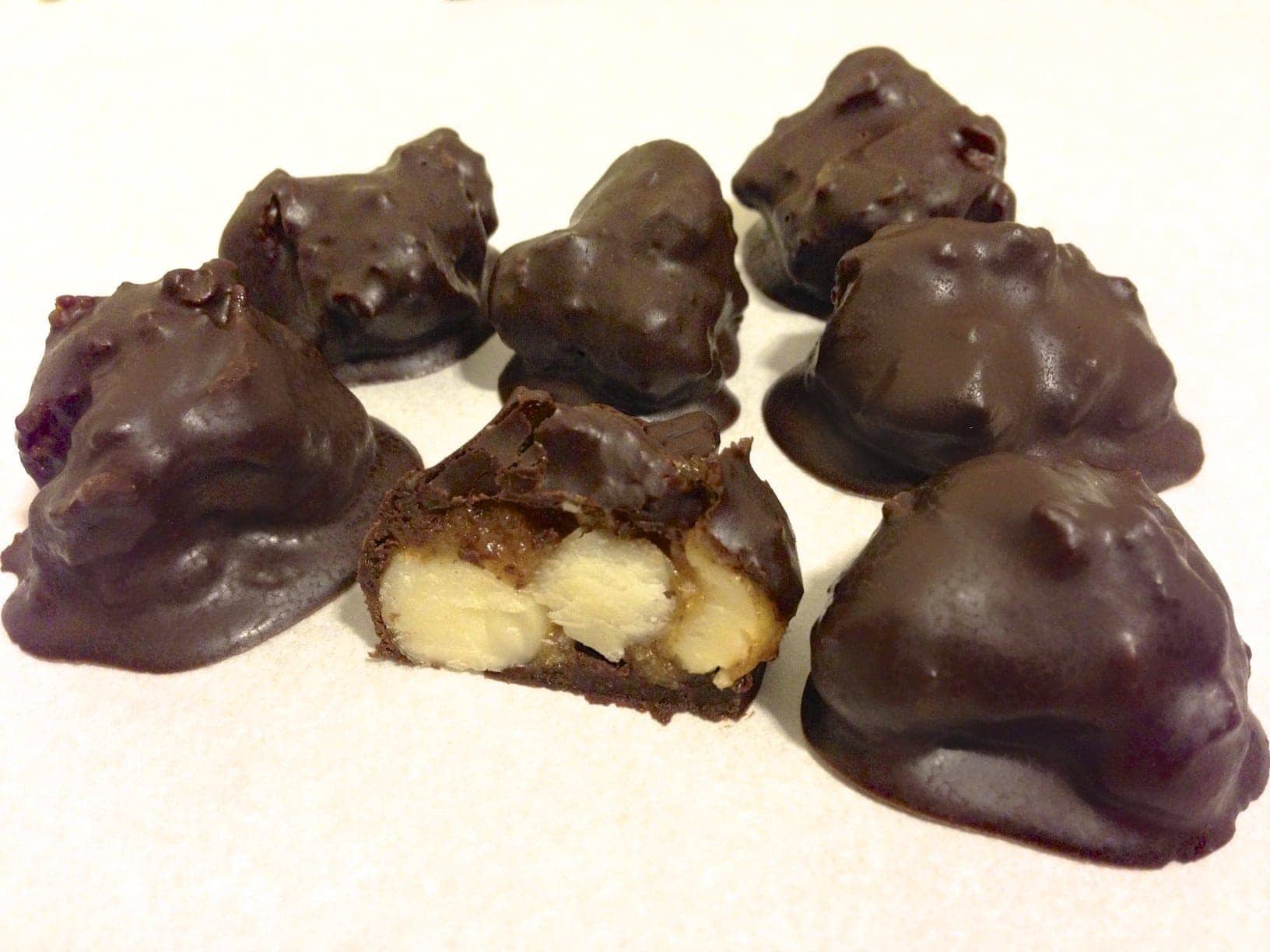 close up of several chocolate covered paleo macadamia nut clusters with one piece cut in half showing the inside texture 