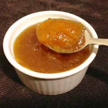 close up of a small white dish with paleo orange marmalade with a spoon inside filled with marmalade
