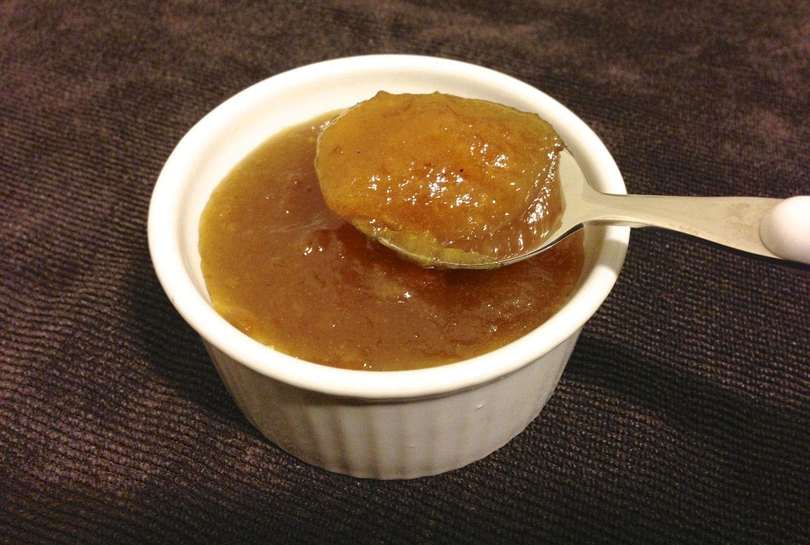 close up of a small white dish with paleo orange marmalade with a spoon inside filled with marmalade 