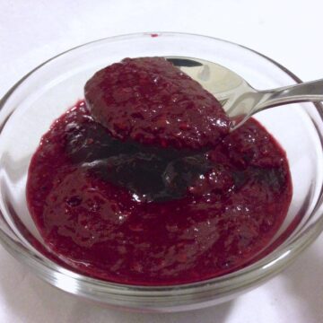 close up of small glass dish filled with sugar free mix berry jam with a spoon inside jam