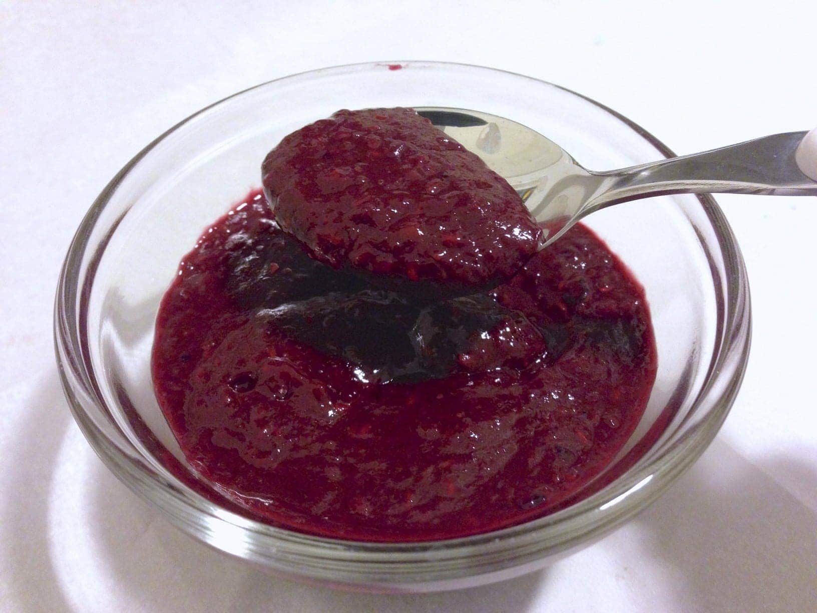 close up of small glass dish filled with sugar free mix berry jam with a spoon inside jam