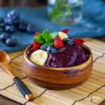 round wooden bowl filled with acai and topped with fresh banana blueberries and strawberries on a bamboo placemat