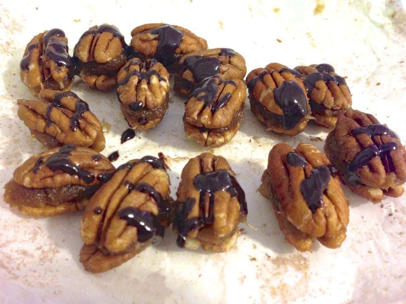 close up of numerous caramel filled pecans drizzled with chocolate