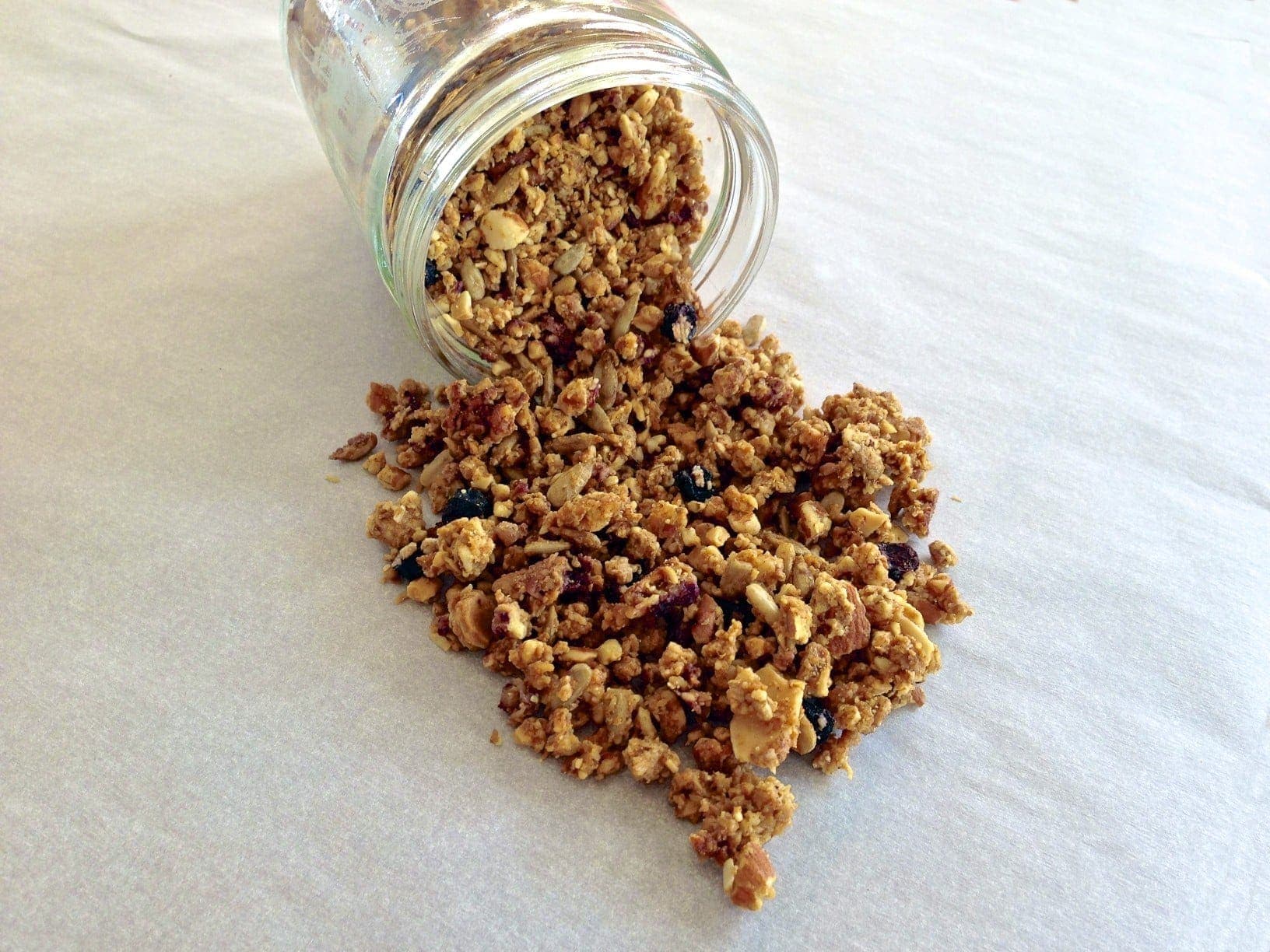 pile of paleo blueberry granola spilling out of a glass jar tipped over on its side