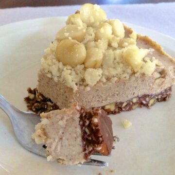 close up of a slice of paleo macadamia nut pie topped with full and chopped nuts and fork in foreground with bite on it