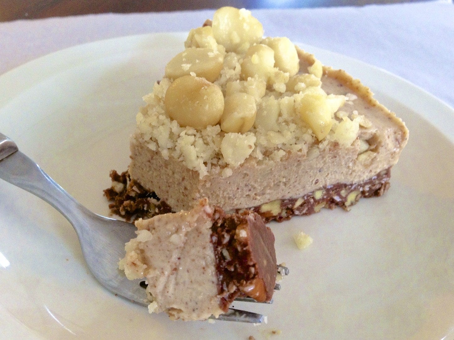 close up of a slice of paleo macadamia nut pie topped with full and chopped nuts and fork in foreground with bite on it