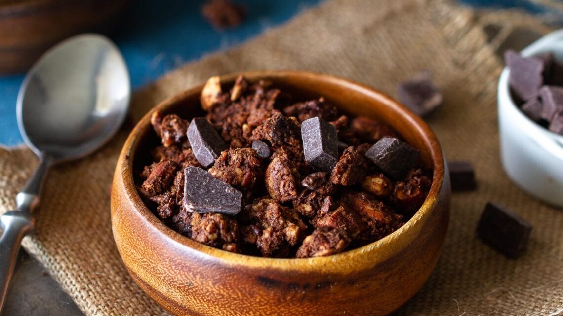 wooden bowl filled with chocolate granola sprinkled with large chocolate chips and a spoon next to it.