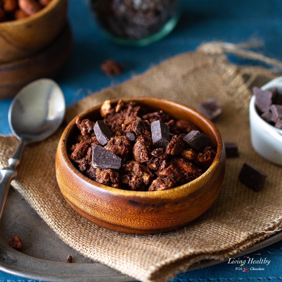 wooden bowl filled with chocolate granola sprinkled with large chocolate chips and a spoon next to it.