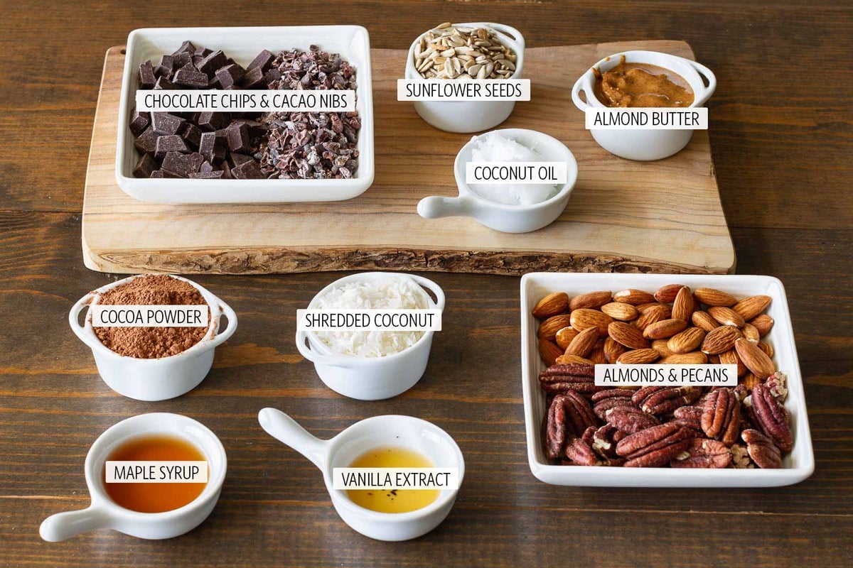 ingredients to make chocolate granola in small white dishes on a wooden table.
