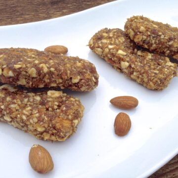 four pieces of paleo apricot lemon energy bars on white plate with a few loose almonds scattered on the plate