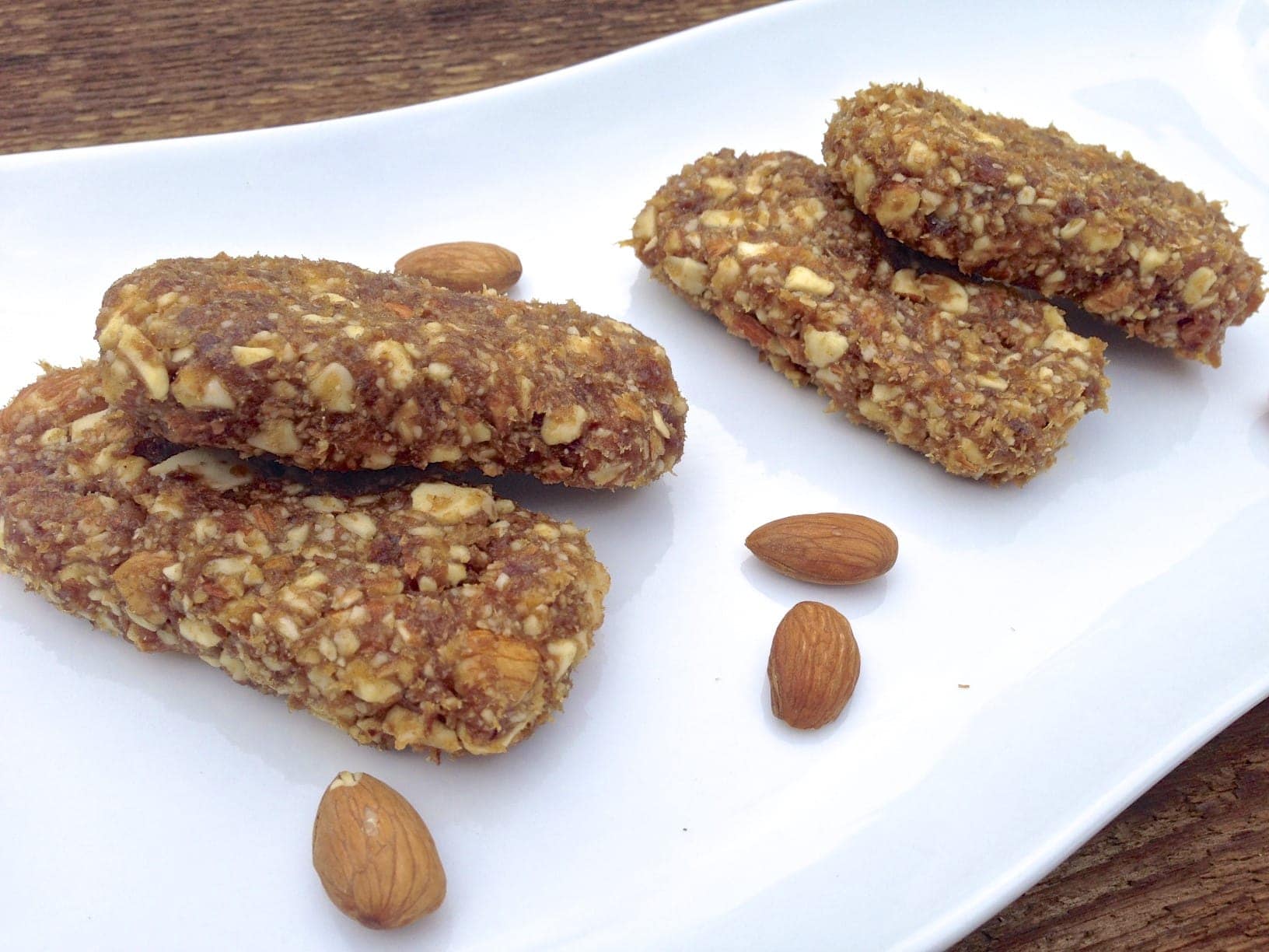 four pieces of paleo apricot lemon energy bars on white plate with a few loose almonds scattered on the plate