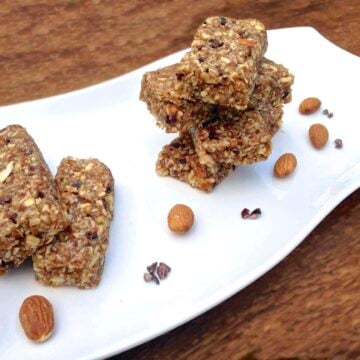 stacked pieces of paleo cacao nibs coconut energy bars on white plate with a few loose almonds scattered on the plate