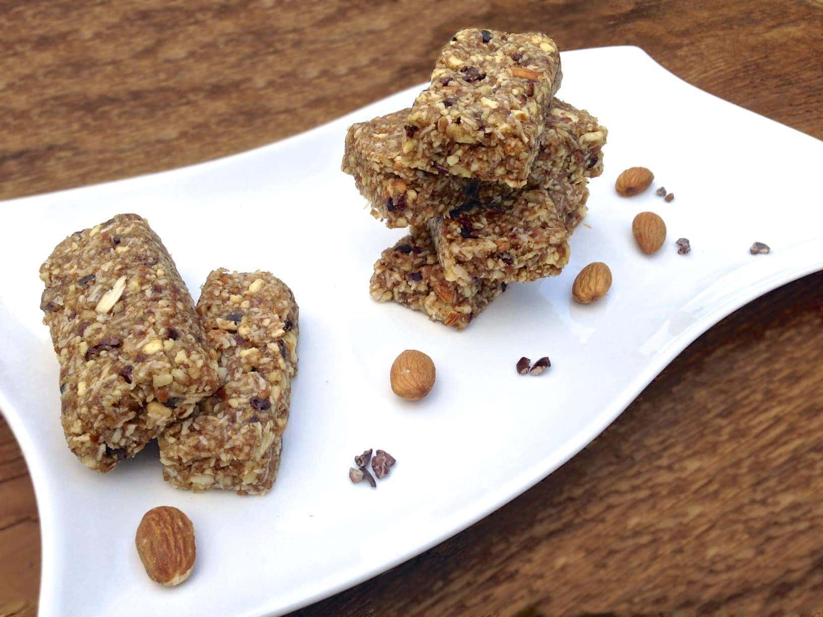 stacked pieces of paleo cacao nibs coconut energy bars on white plate with a few loose almonds scattered on the plate