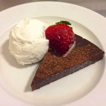 slice of chocolate cake topped with a single strawberry with a scoop of paleo coconut vanilla ice cream beside the cake