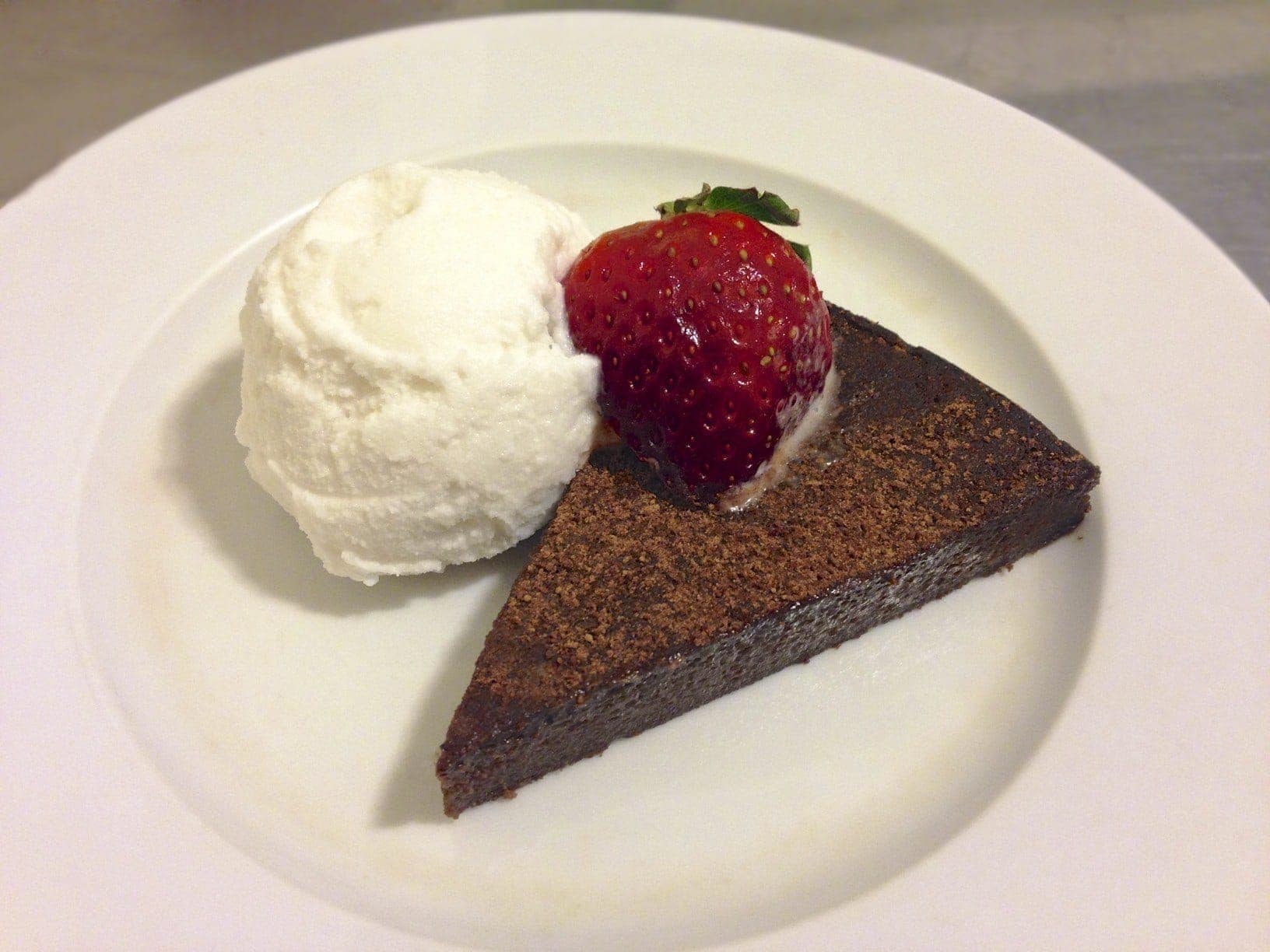 slice of chocolate cake topped with a single strawberry with a scoop of paleo coconut vanilla ice cream beside the cake