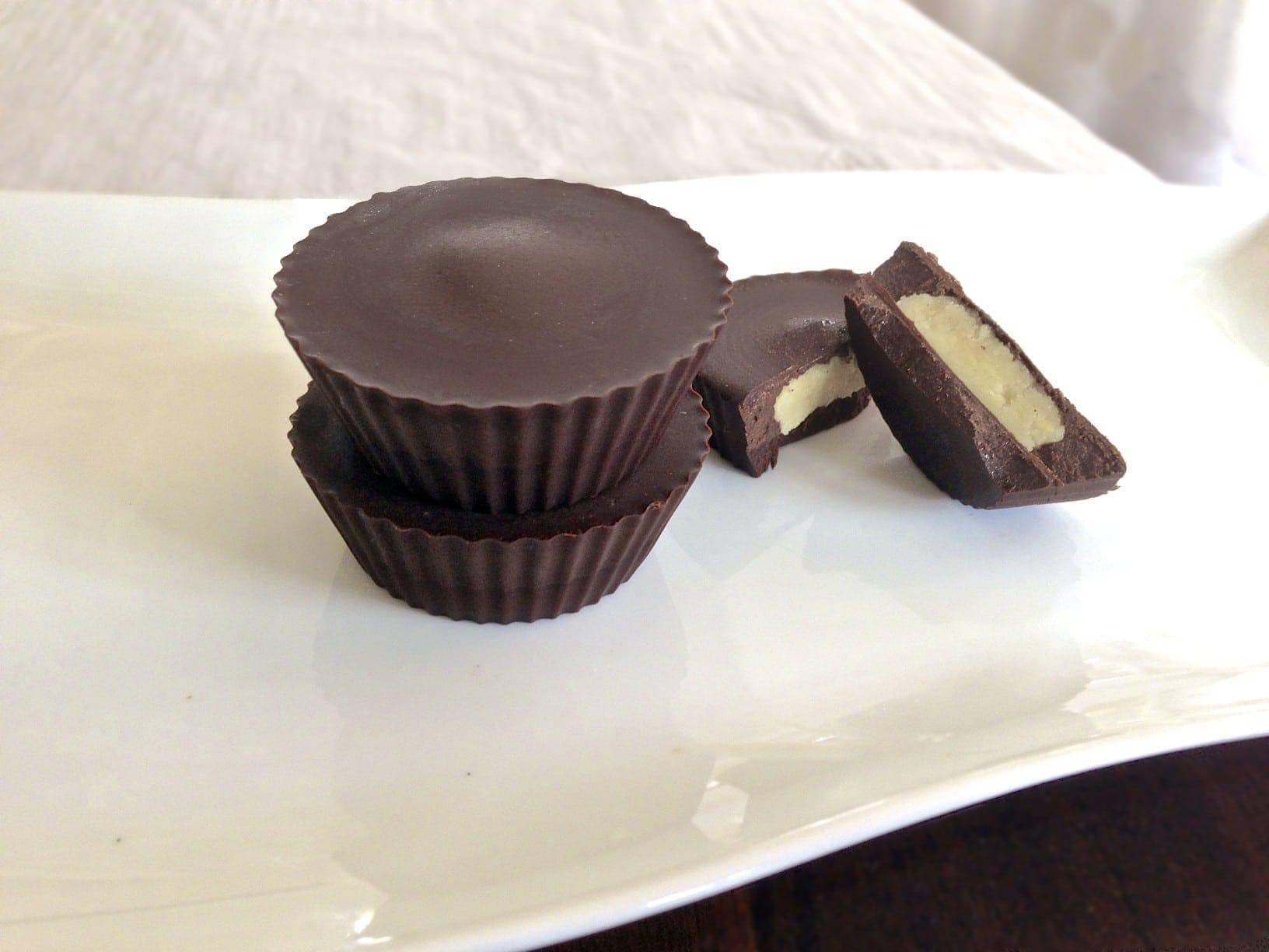 plate with stack of two paleo macadamia nut butter cups and one cup broken in half showing texture inside 