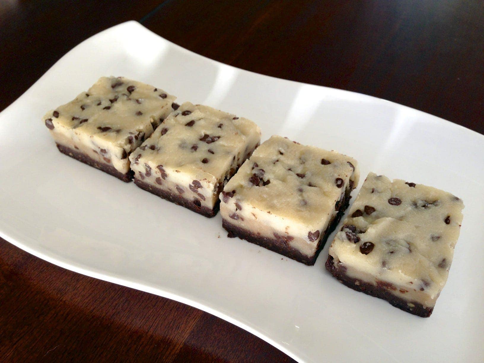 four square pieces of raw no bake chocolate chip cookie dough brownies on white plate with dark background 