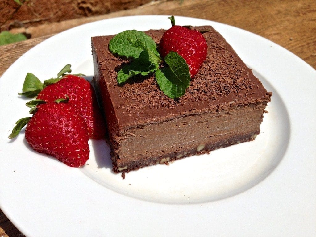 large square piece of chocolate truffle pie topped with fresh mint and a single strawberry and two loose strawberries on side