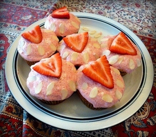 plate of paleo strawberry almond cupcakes topped with frosting and a slice of strawberry