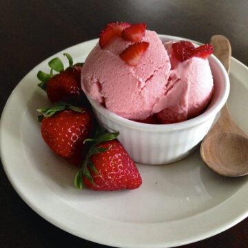 small white serving dish with strawberry frozen yogurt topped with diced strawberries and three strawberries on side