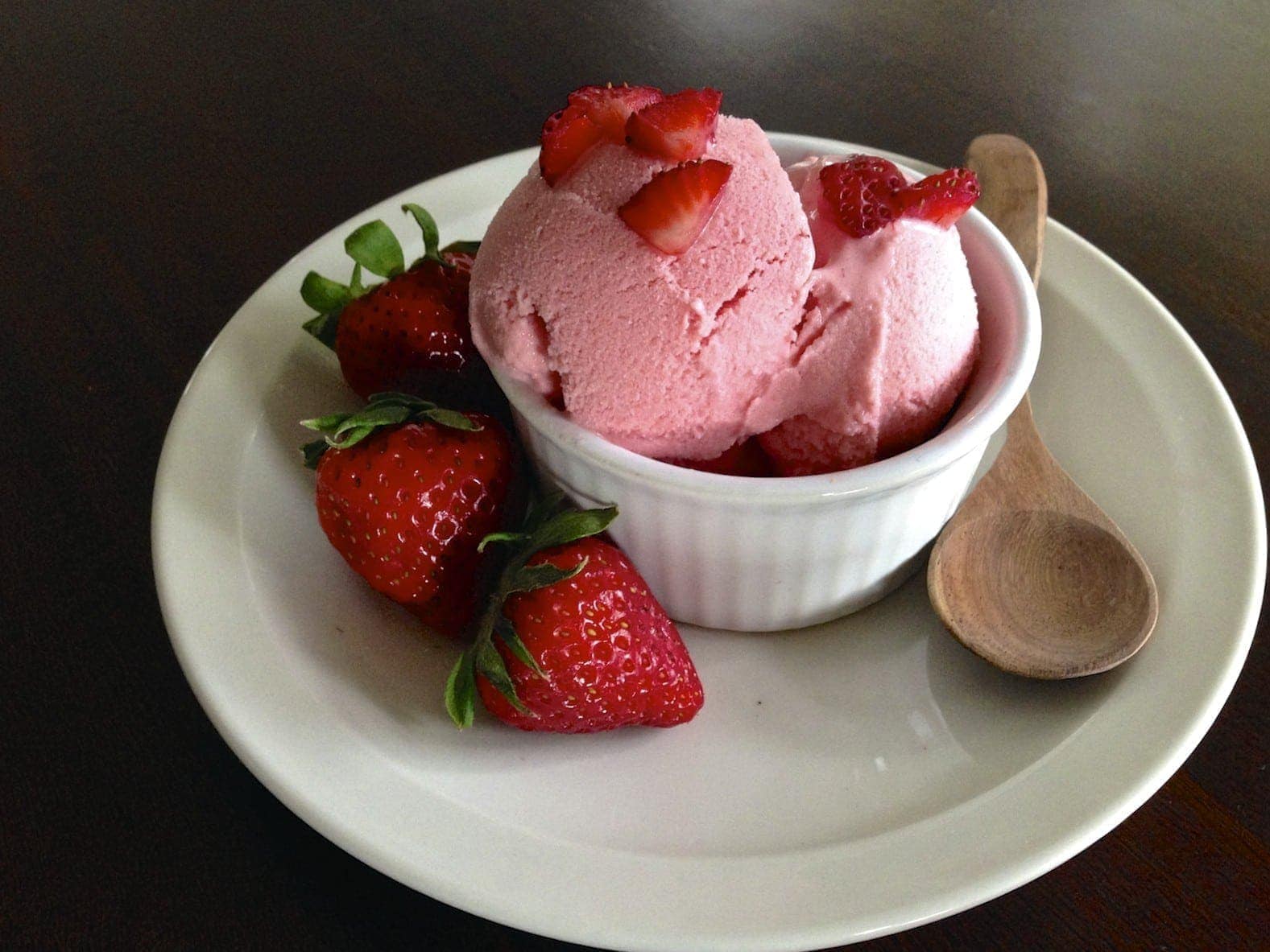small white serving dish with strawberry frozen yogurt topped with diced strawberries and three strawberries on side 
