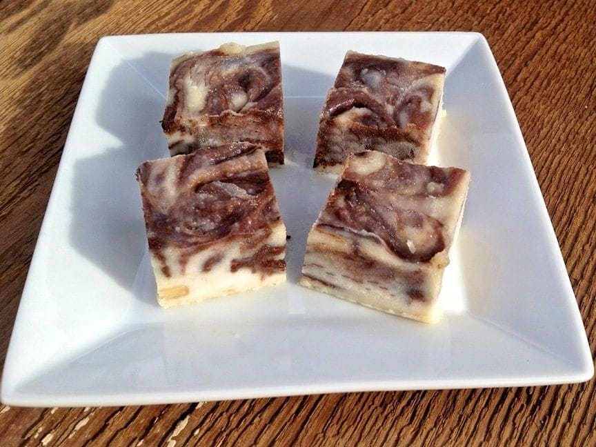 four pieces of macadamia nut butter chocolate swirl fudge bites on a white plate on top of wooden table