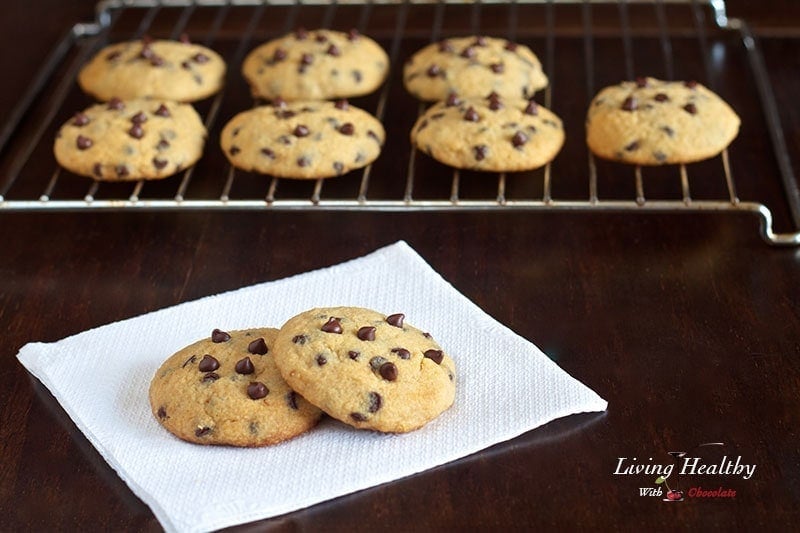 paleo chocolate chip cookies cooling on a wire rack in background with two cookies in foreground on white napkin 