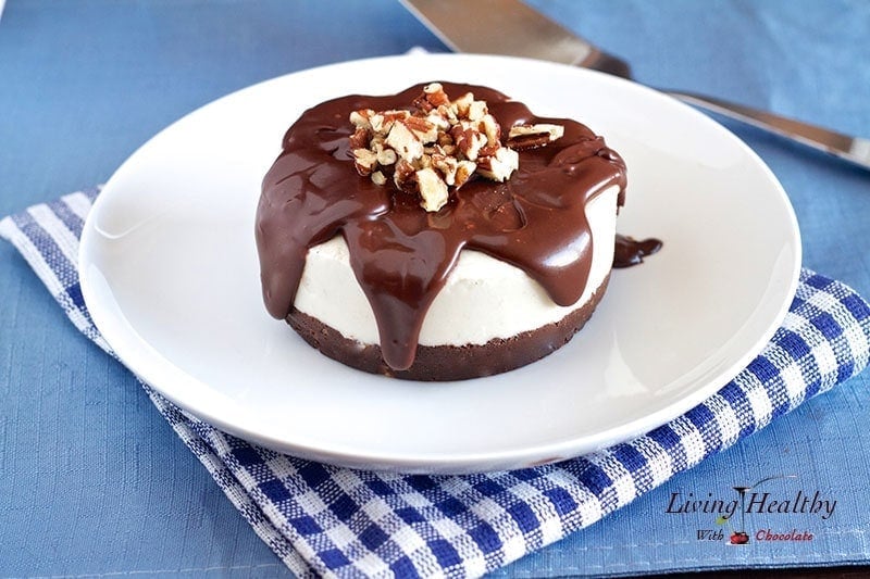 white plate with paleo brownie ice cream cake topped with melted chocolate and chopped nuts with blue napkin